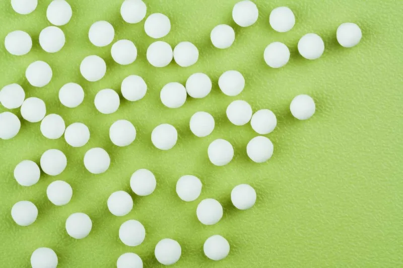 homeopathic pills background - overhead horizontal view of homeopathic medicinal pills (made from an inert substance - sugar lactose) spillage on a green tabletop