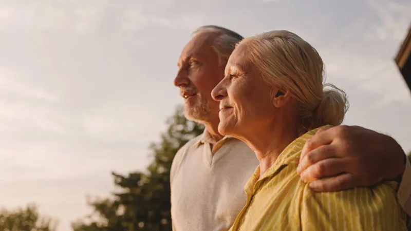 smiling aged couple hugging outdoors, enjoying city view at sunset, family love