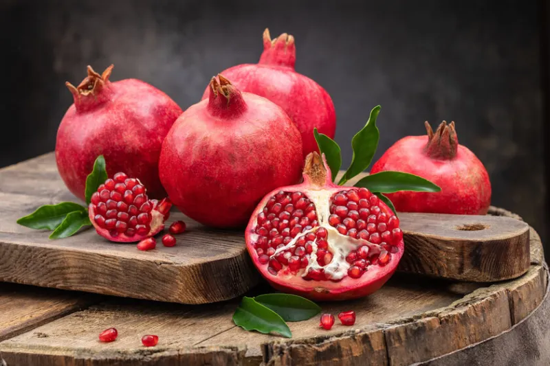 healthy pomegranate fruit with leaves and open pomegranate on an old wooden board, side view, dark vintage background