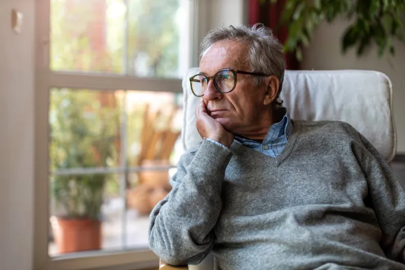 senior man looking out of window at home