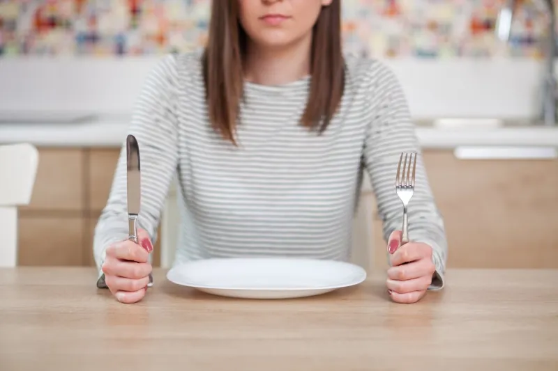 displeased young woman sitting at the empty plate shallow depth of field, focus on foreground