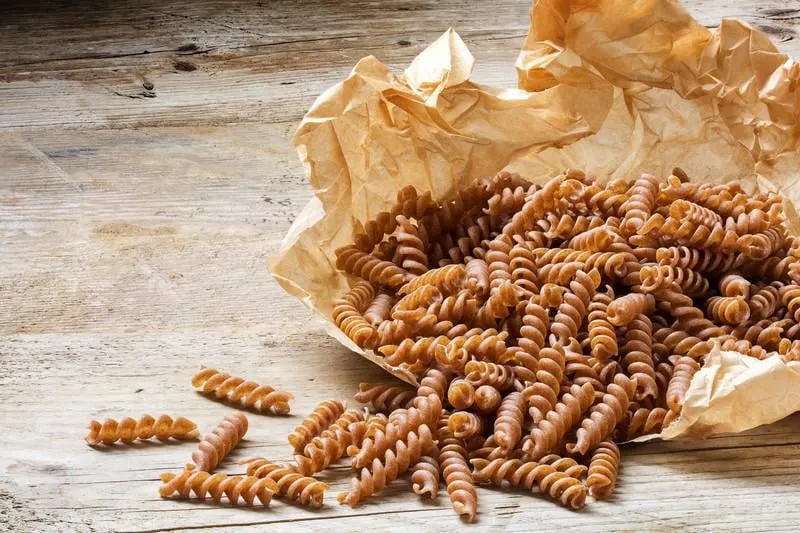 épeautre entier fusilli de grains entiers organiques orthographiés tombant d'un sac en papier sur une table en bois rustique, copie espace