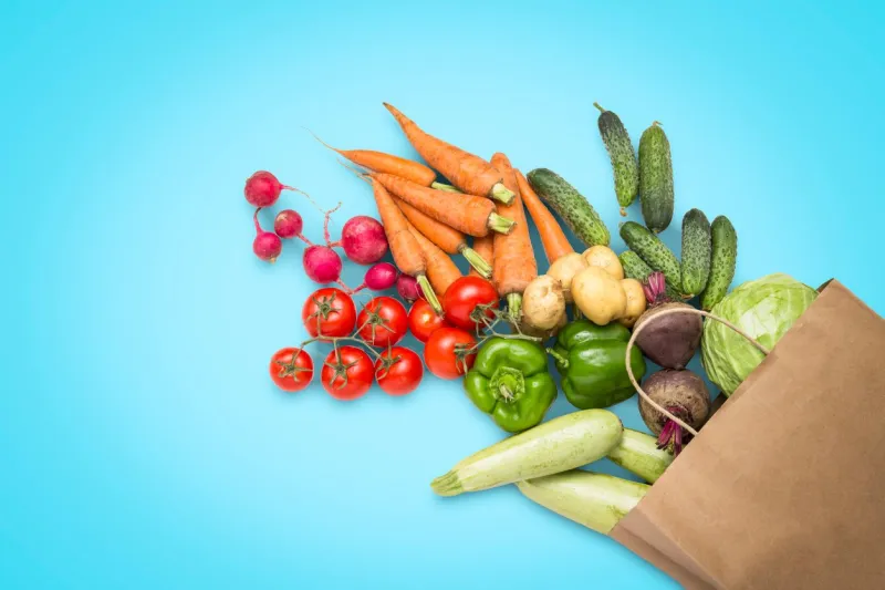 paper shopping bag and fresh organic vegetables on a blue background concept of buying farm vegetables, taking care of health, vegetarianism country style, farm fair flat lay, top view