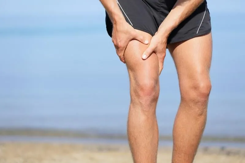 blessure musculaire homme avec une entorse muscles de la cuisse athlète dans un short de sport serrant ses muscles de la cuisse après les avoir tirés ou tendus en faisant du jogging sur la plage