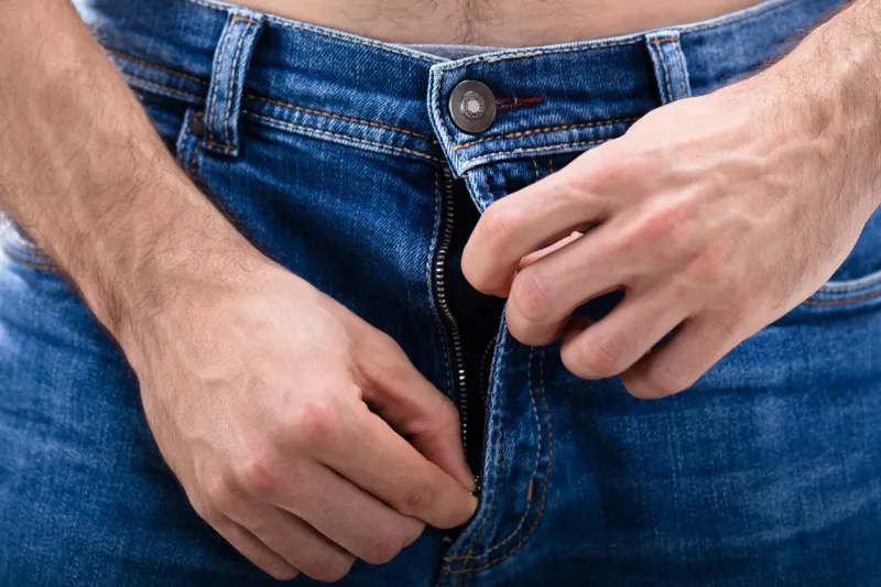 close-up of a man's hand unzipping the blue jeans