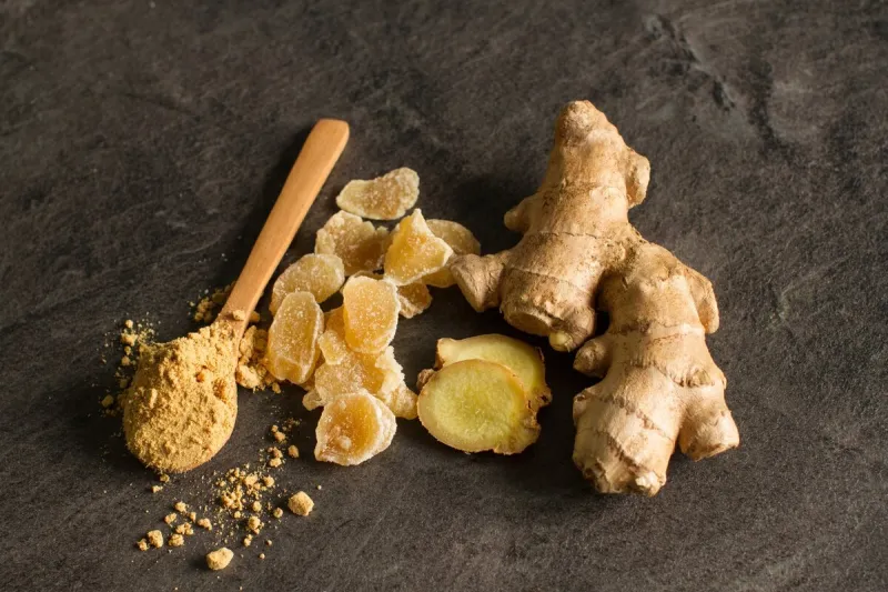 ginger root, candied and ginger powder in wooden spoon over grey