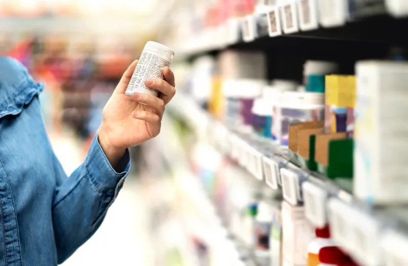 customer in pharmacy holding medicine bottle woman reading the label text about medical information or side effects in drug store patient shopping pills for migraine or flu vitamin or zinc tablets