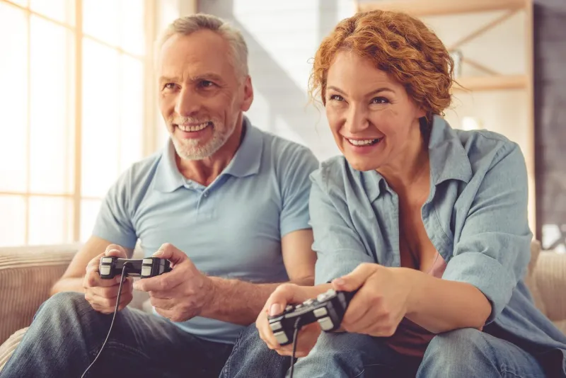 beau couple mature heureux joue console de jeu et souriant tout en étant assis sur le canapé à la maison