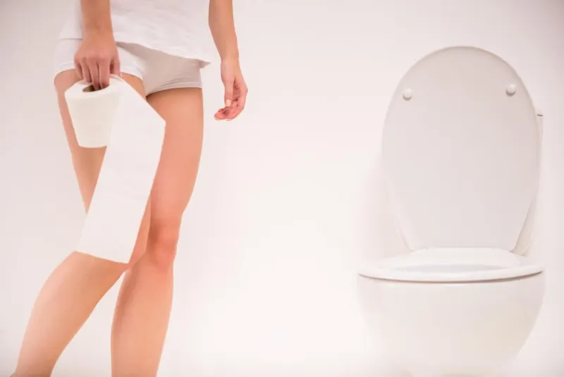 en utilisant les toilettes une jeune femme utilise une toilette avec un rouleau de papier toilette à la main