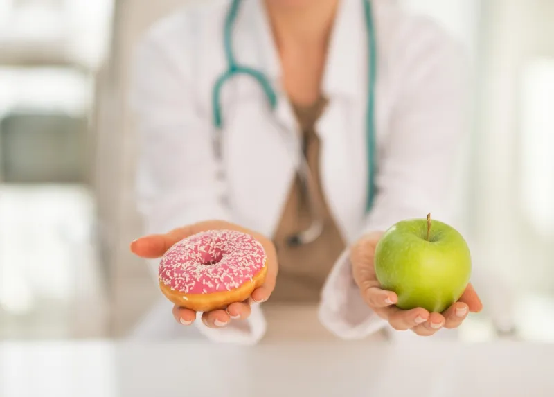 gros plan sur une femme médecin donnant un choix entre pomme et beignet