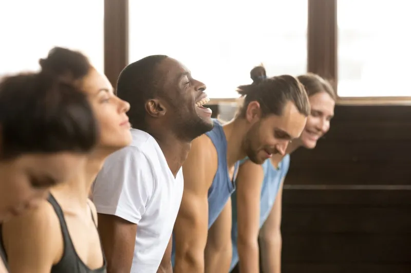 african man beginner laughing having fun trying to do yoga pose, push ups plank or stretching in upward facing dog exercise at group training class with multiracial diverse people, closeup side view
