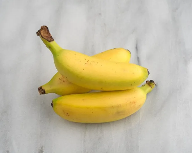 a group of a small bananas on a marble cutting board illuminated with natural light