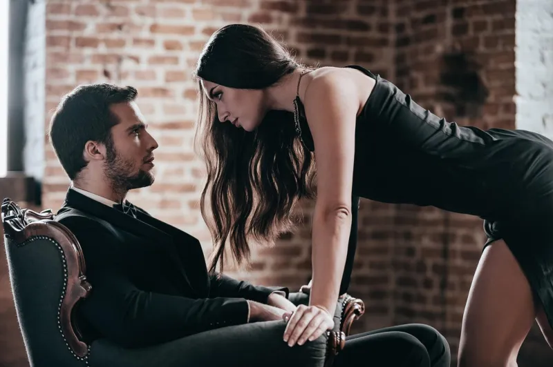 belle jeune femme en robe de cocktail se penchant vers son petit ami assis dans une chaise tout en se regardant dans l'intérieur de loft