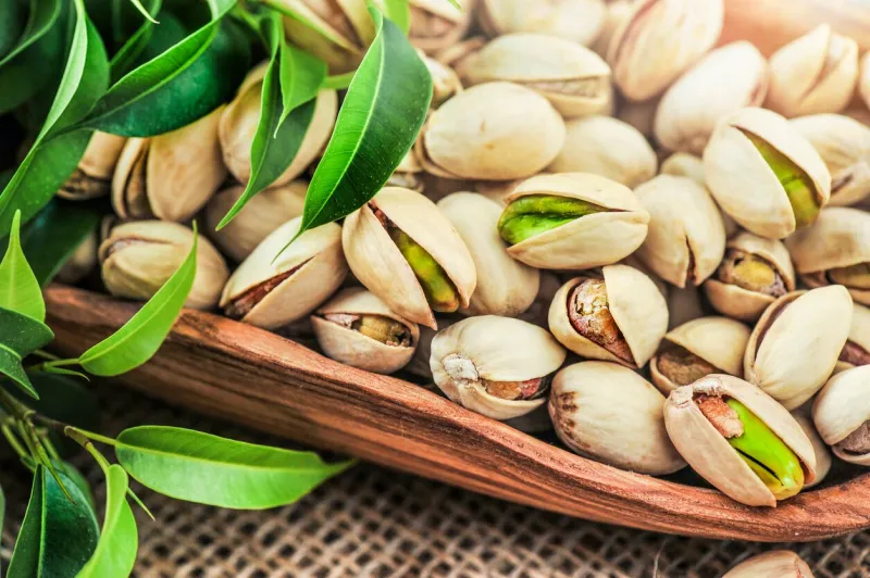 bowl with pistachios nut on a wooden table with green leaves pistachio nuts detail