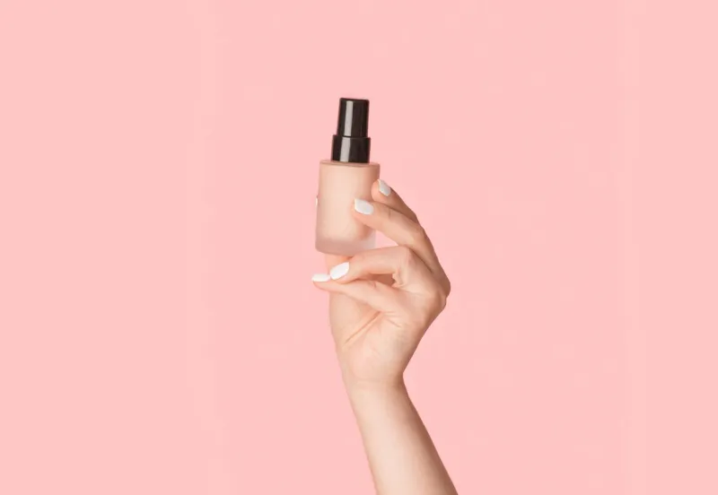 skin care concept millennial lady holding bottle of natural concealer on pink background, close up