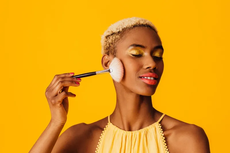 portrait of a beautiful young woman applying cover up loose powder to her cheeks with a makeup brush, eyes closed