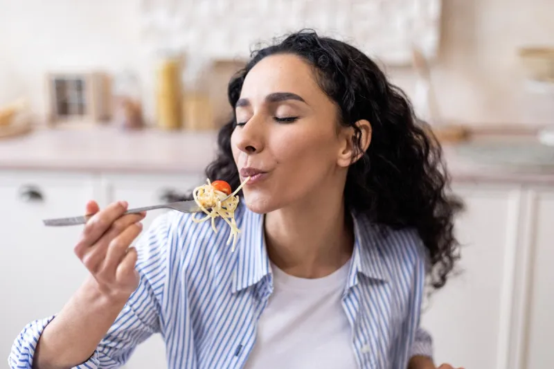 delicious meal hungry young woman eating tasty domestic spaghetti, sitting at table in kitchen interior and enjoying homemade food