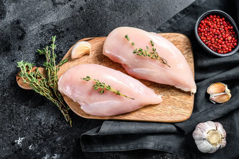 raw chicken breast fillet on a chopping board with herbs and spices black background top view