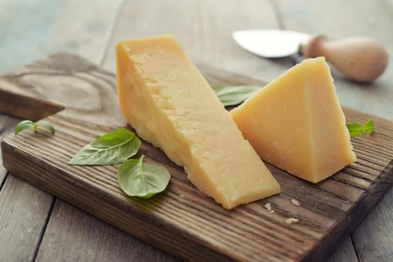 fromage parmesan sur planche à découper au basilic et couteau sur fond en bois