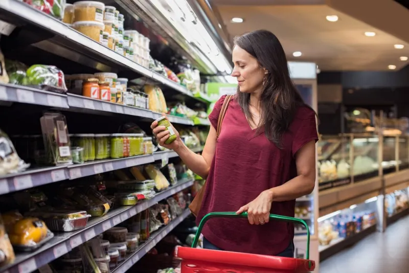 young woman shopping in grocery store mature woman checking food label in supermarket latin woman holding shopping basket and choose a product in supermarket