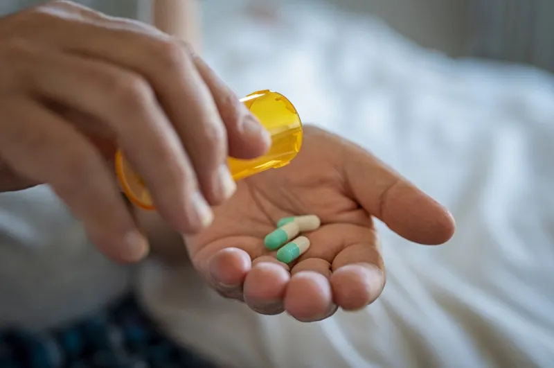 closeup of man hand pouring capsules from a pill bottle into hand senior man taking daily medicine to consume close up of male hands taking daily dose of drug
