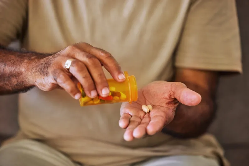medicine, healthcare and pills in the hands of a senior man sitting on a sofa in the retirement home prescription, medication and antibiotics for chronic treatment and wellness with a pensioner