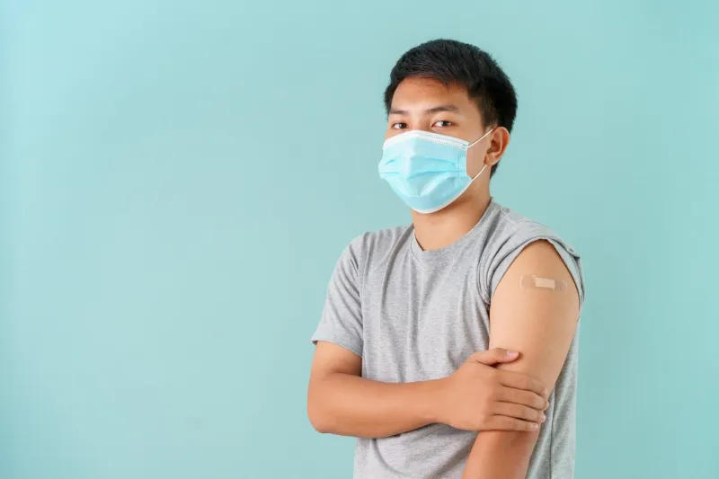 asian men wearing face mask vaccinated showing arm bandage to protect covid-19 spread on blue background