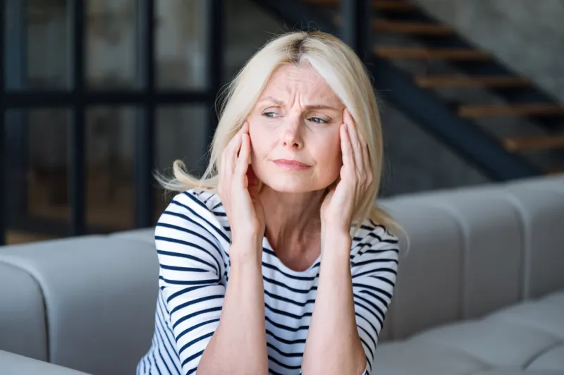 frustrated middle aged woman sitting on couch at home, touching head, suffering from headache stressed upset mature female thinking of health problems mental disorder and memory loss concept