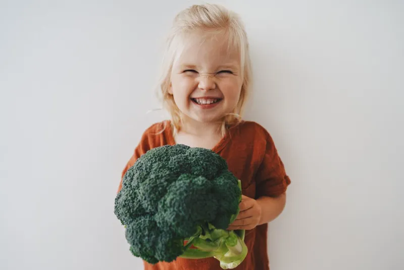 child girl with broccoli healthy food vegan eating lifestyle organic vegetables plant based diet nutrition funny kid happy smiling