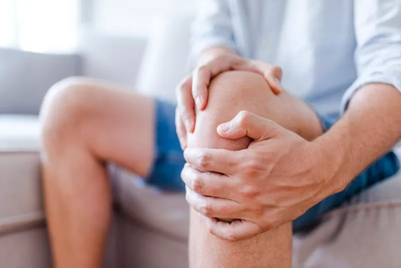 man suffering from knee pain sitting sofa a mature man massaging his painful knee man suffering from knee pain at home, closeup pain knee