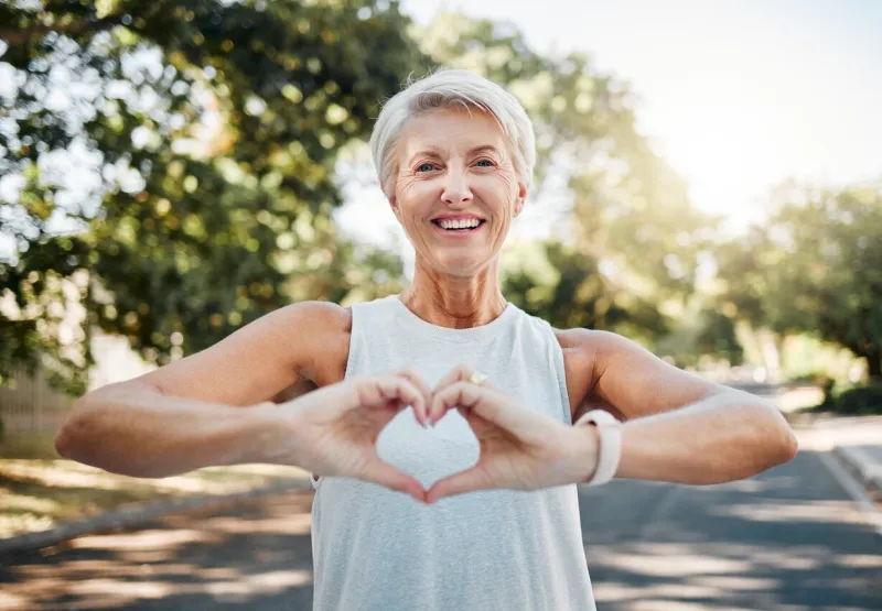 fitness, happy and heart hands of old woman in nature after running for health, wellness and workout smile, motivation and peace with senior lady and sign for love, faith and training in nature