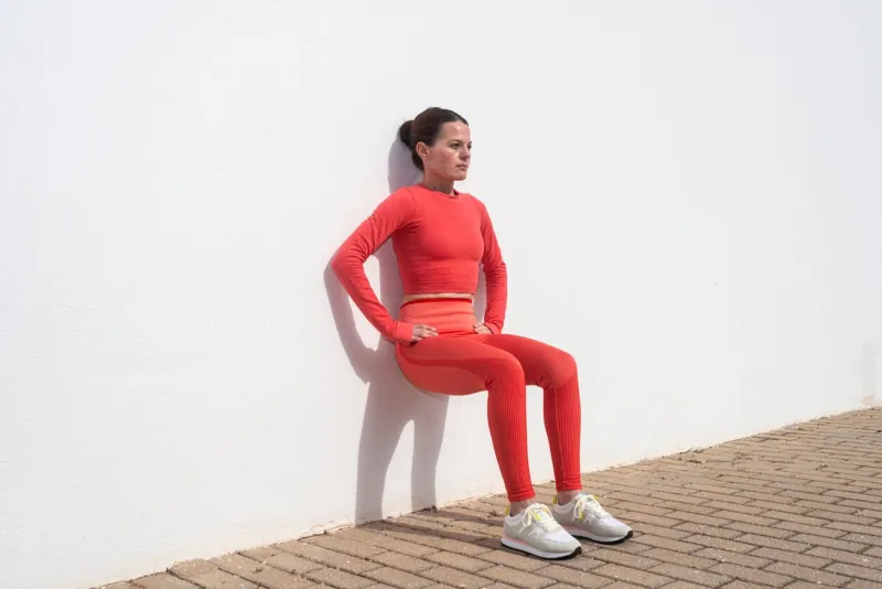 sporty woman doing squats against a white wall outside in the sun