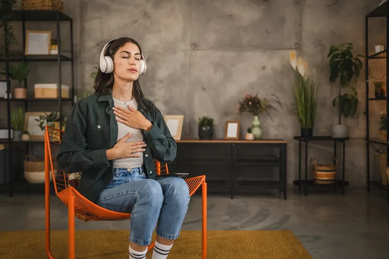 adult woman sit on chair and have guided meditation on headphones