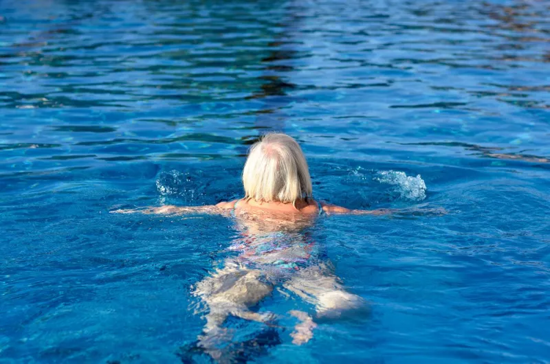 active senior woman swimming in a pool moving away from the camera doing breaststroke in a health and fitness and retirement concept