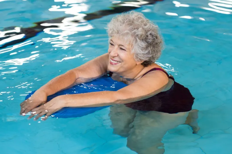 happy senior woman with kickboard in a swimming pool old woman swimming in water with the help of a kickboard smiling old woman swimming with inflatable board in swimming pool