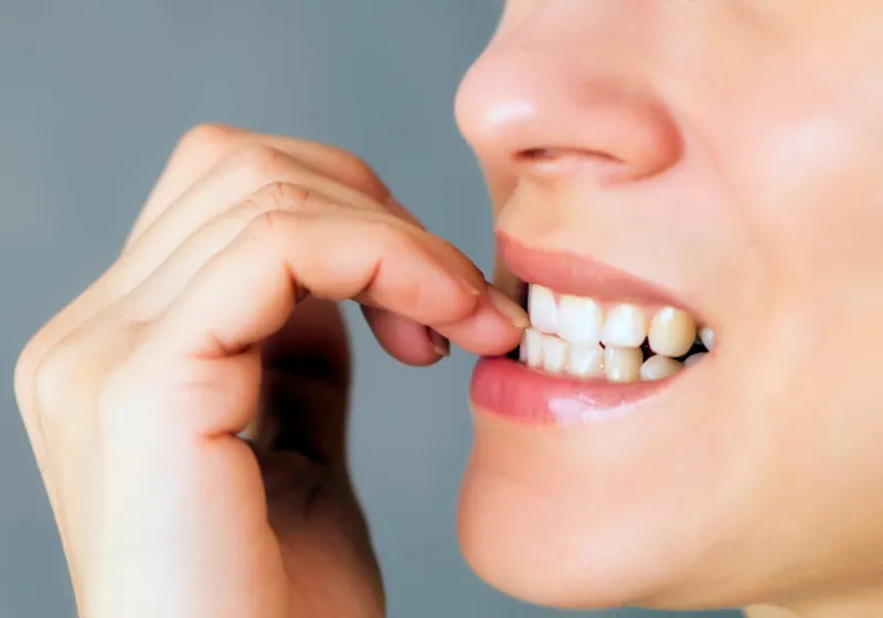 nervous young woman biting her nails on gray background