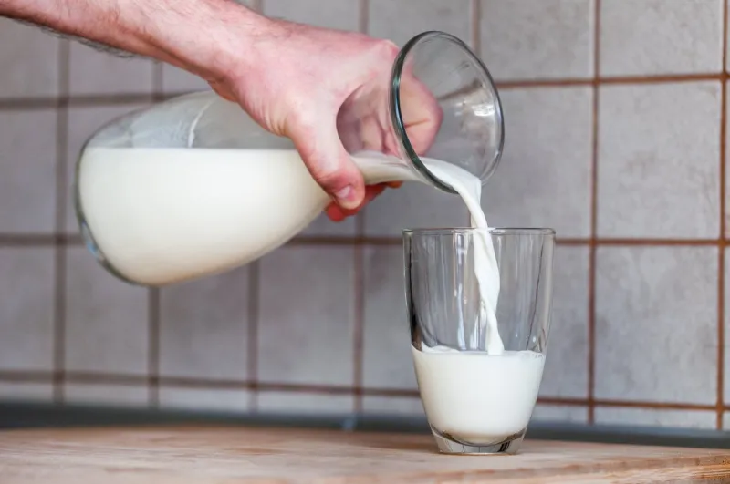 a man's hand holds a jug and pours milk into a glass