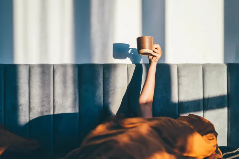 hand holding a cup of coffee while lying on bed morning concept