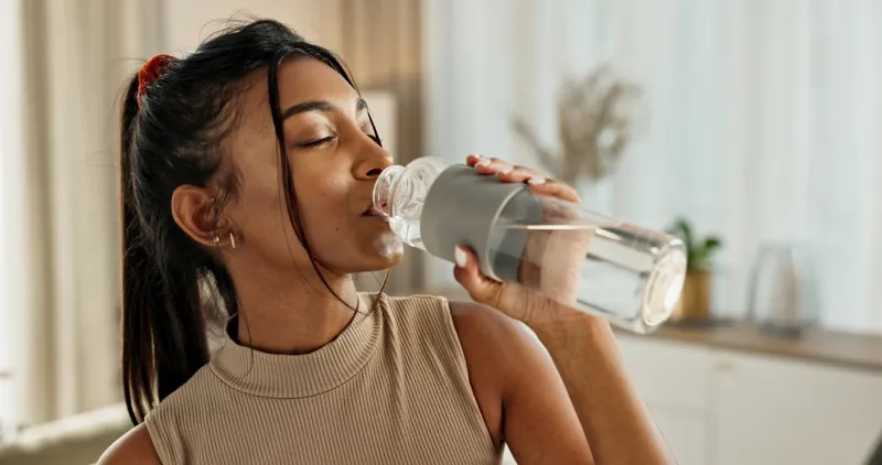 drinking water, yoga or indian woman in home with health, fitness or wellness for natural hydration thirsty female person, tired or healthy girl with liquid bottle after pilates to detox or relax