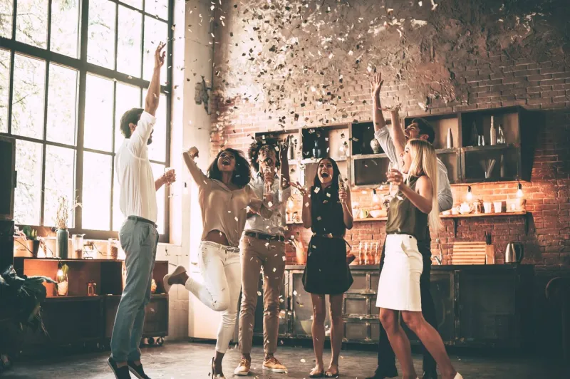 full length of cheerful young people throwing confetti and jumping while enjoying home party on the kitchen
