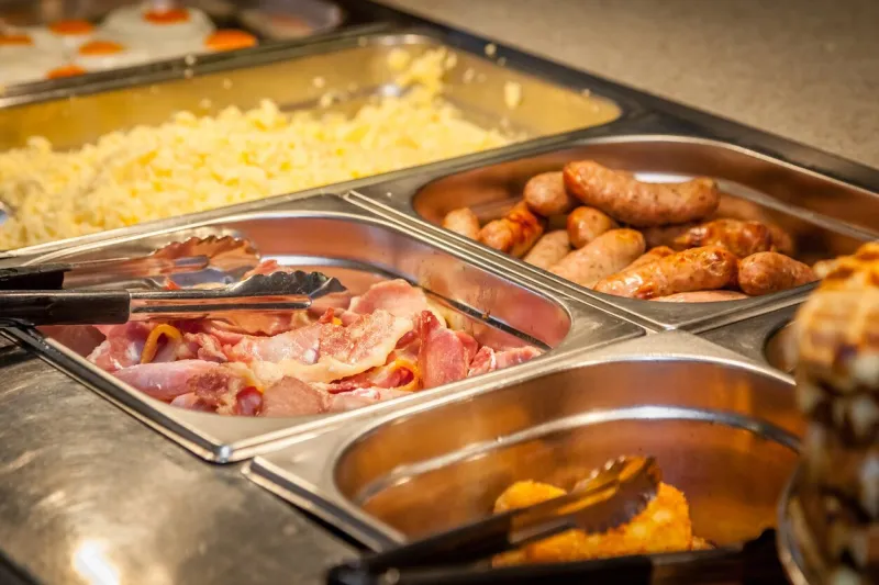 hot counter containing warm breakfast items such as scrambled or fried eggs, bacon, sausages, grilled tomatoes