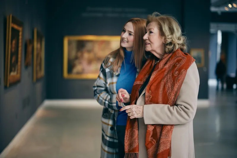grandmother and adolescent granddaughter are looking at the paintings in the art gallery
