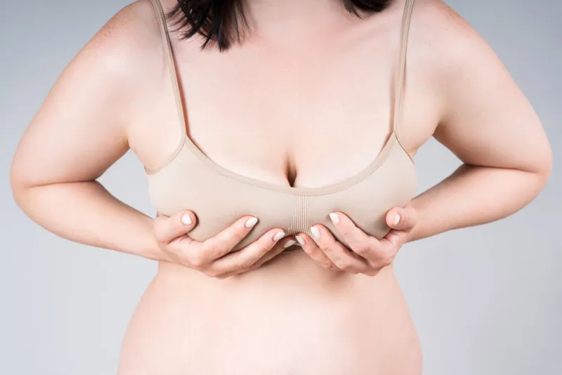 breast test, woman in beige bra examining her breasts for cancer on gray studio background
