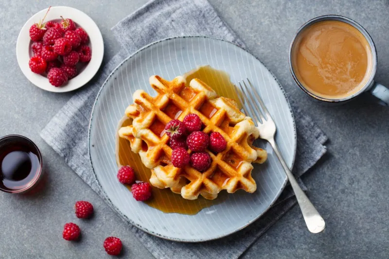 fresh waffles with cup of coffee and raspberry grey background top view