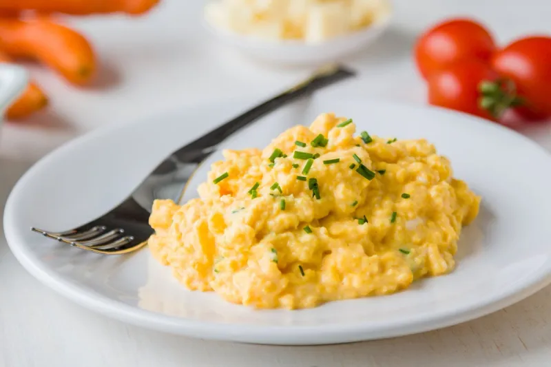 fresh scrambled eggs on white plate on breakfast table