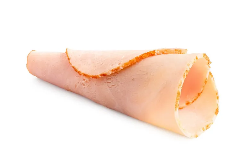 a rolled up single slice of chicken ham isolated on white