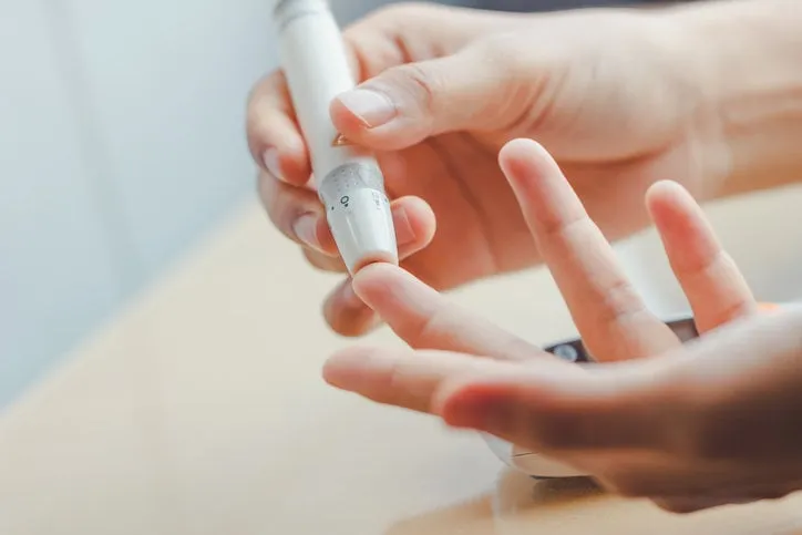 close up of woman hands using lancet on finger to check blood sugar level by glucose meter using as medicine, diabetes, glycemia, health care and people concept