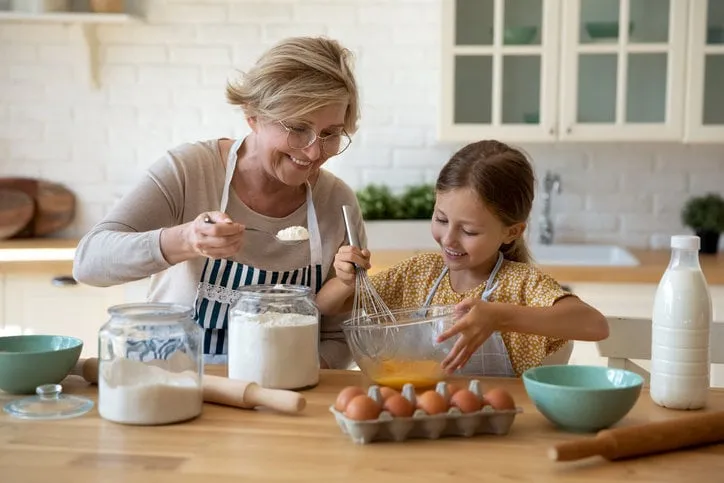 cooking with soul happy little girl in apron help senior grandma at kitchen mix dough for cookies pancakes smiling older granny teach small grandkid to bake homemade cake pastry share family recipe