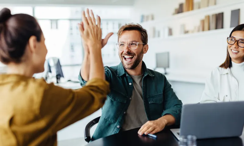 successful business people giving each other a high five in a meeting two young business professionals celebrating teamwork in an office