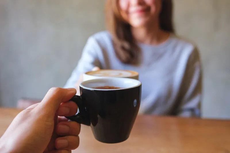 closeup image of a couple people clinking coffee cups together in cafe